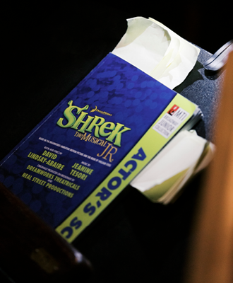 A program for 'Shrek The Musical Jr.' rests on a chair.